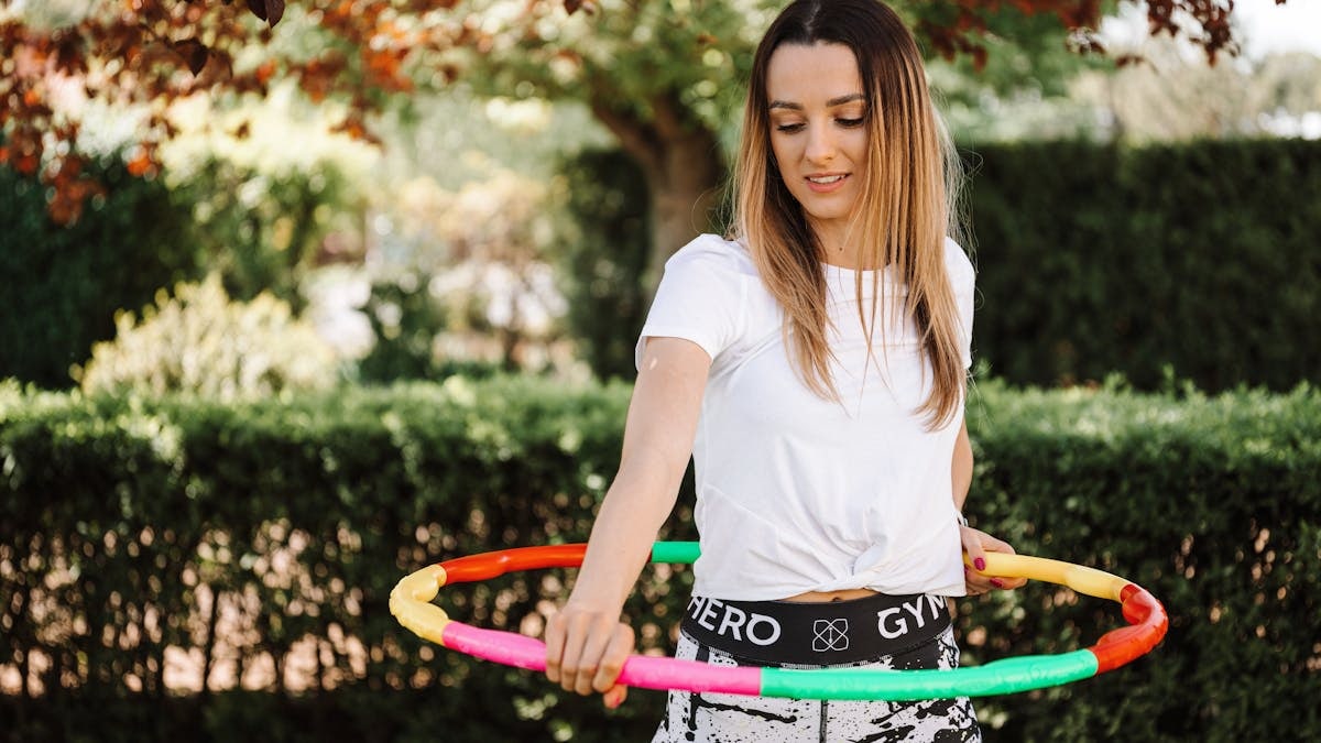 A fit woman enjoying a hula hoop workout in a sunny garden setting.